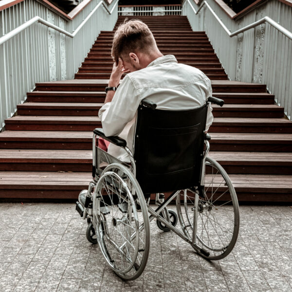 Many stairs. Horizontal image of depressed disabled man sitting in the wheelchair and facing the difficulties with climbing the stairs alone