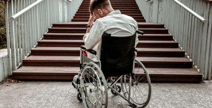 Many stairs. Horizontal image of depressed disabled man sitting in the wheelchair and facing the difficulties with climbing the stairs alone